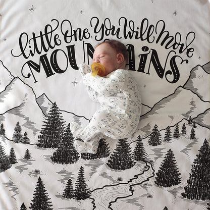 a baby is sleeping on a blanket with mountains and trees